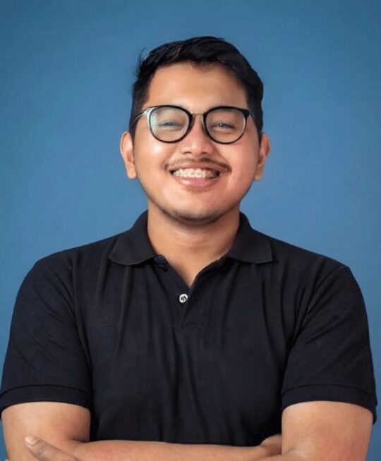Ahmad Thariq Syauqi, founder of Uply Meet, smiling with arms crossed in front of a blue background