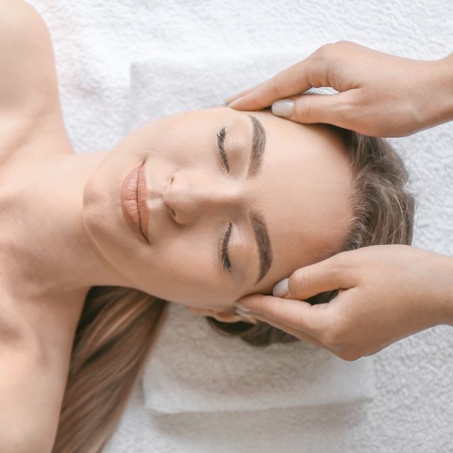 Therapist giving a calming head massage to a client lying on white towels